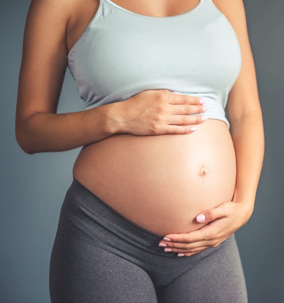 Young pregnant woman, with casual clothes touching her bare tummy