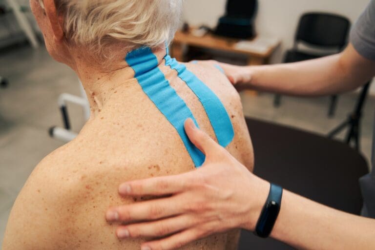 Medical worker adjusting blue kinesiology tape on aging person back with his thumbs during treatment