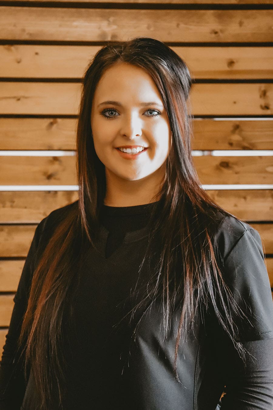Chiropractic Technician Brooke Papenfuss, a smiling woman in a black long-sleeved shirt with long auburn hair